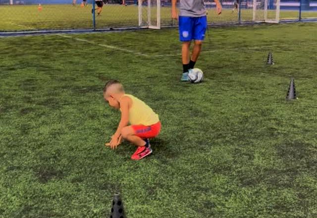Criança agachada junto ao cone durante atividade do baby fut